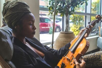 Elegant woman with turban practicing violin in cozy indoor setting.
