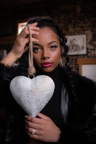 Portrait of a woman indoors holding a heart-shaped ornament, exuding elegance.