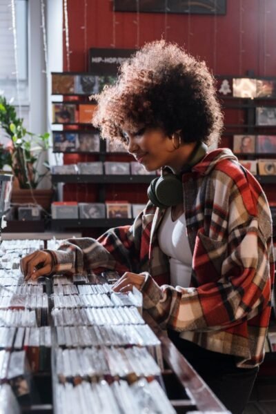 Curly-haired woman in a plaid shirt exploring compact discs at a music store.