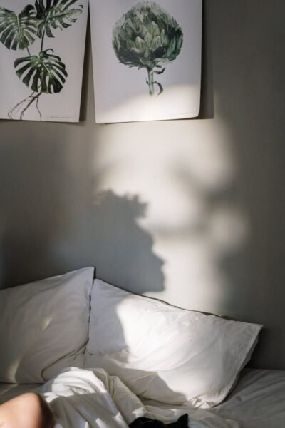 Sunlight casts shadows on bed and wall art in a cozy bedroom.