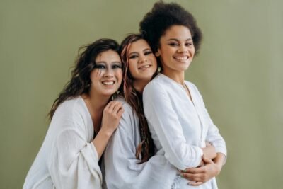 Three diverse women smiling and embracing, symbolizing unity and friendship.