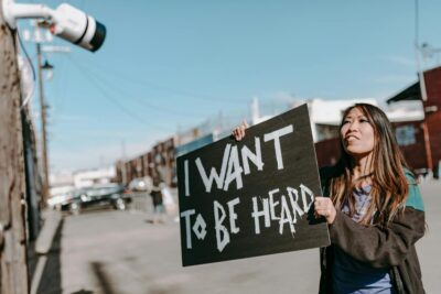 A woman holds a sign reading 'I want to be heard' during a protest on a sunny city street.
