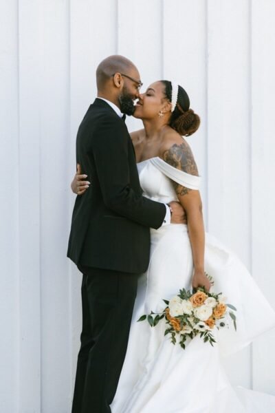 A bride and groom kissing in front of a white wall