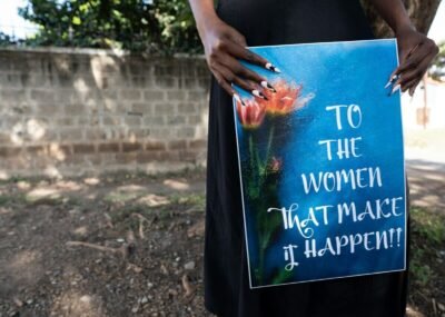 Woman holds sign "to the women that make it happen!!"