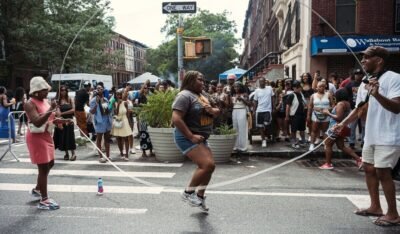 Joyful scene at a lively Brooklyn block party with people enjoying jump rope and street festivities.