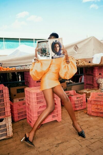 A person in a yellow dress holding a Vogue magazine in a market