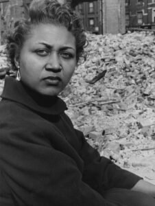Woman with serious expression in front of rubble