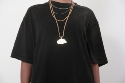 Black t-shirt with layered gold necklaces and a cap pendant
